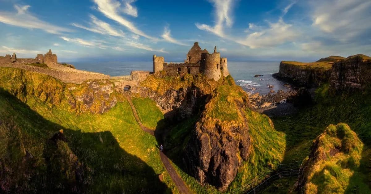 A landscape portrait of beautiful Ireland with a castle sitting cliffside. The sun is setting, highlighting the castle.