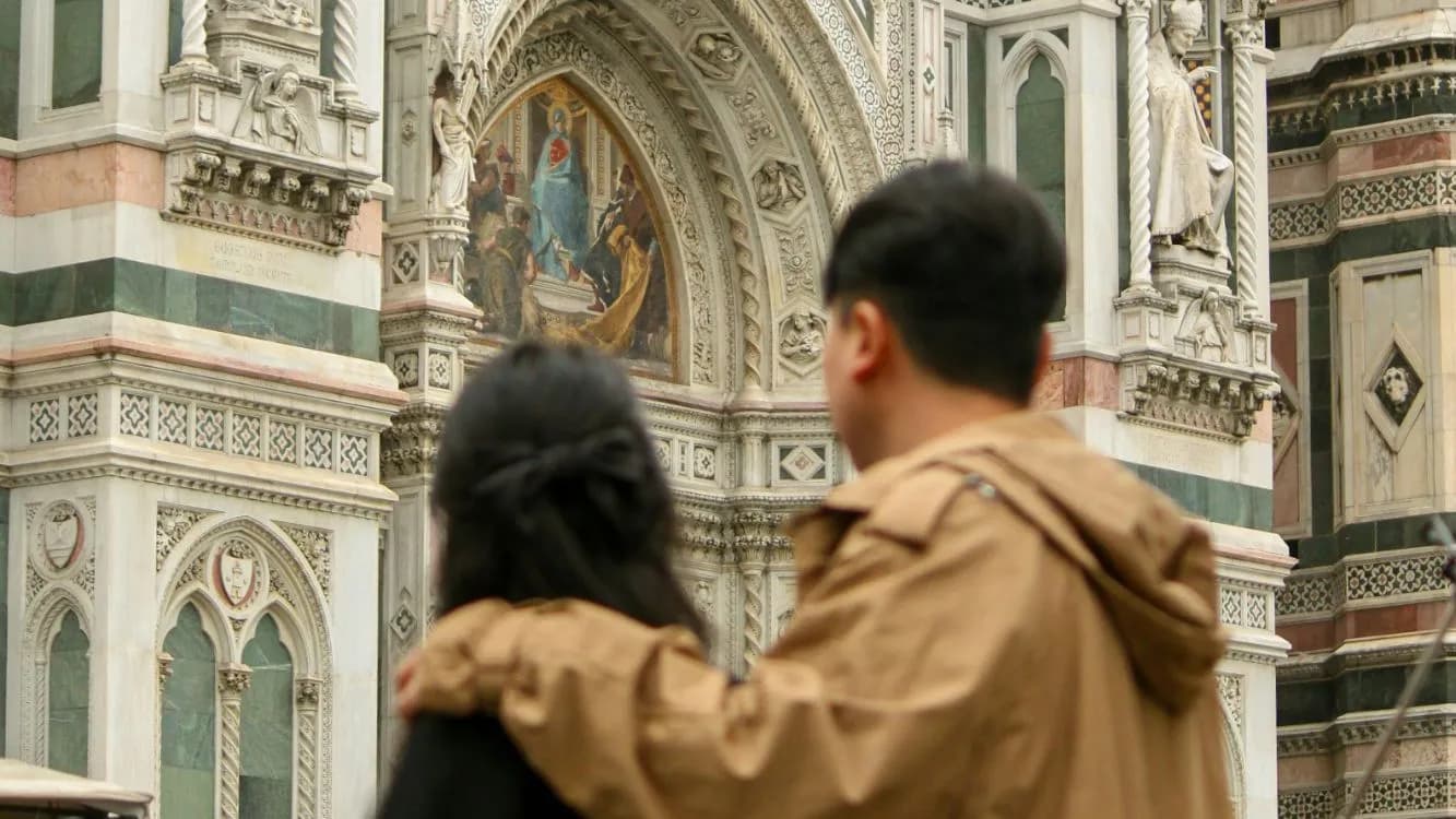 A couple arm in arm admiring the marble facade and mosaic portal of Florence Cathedral