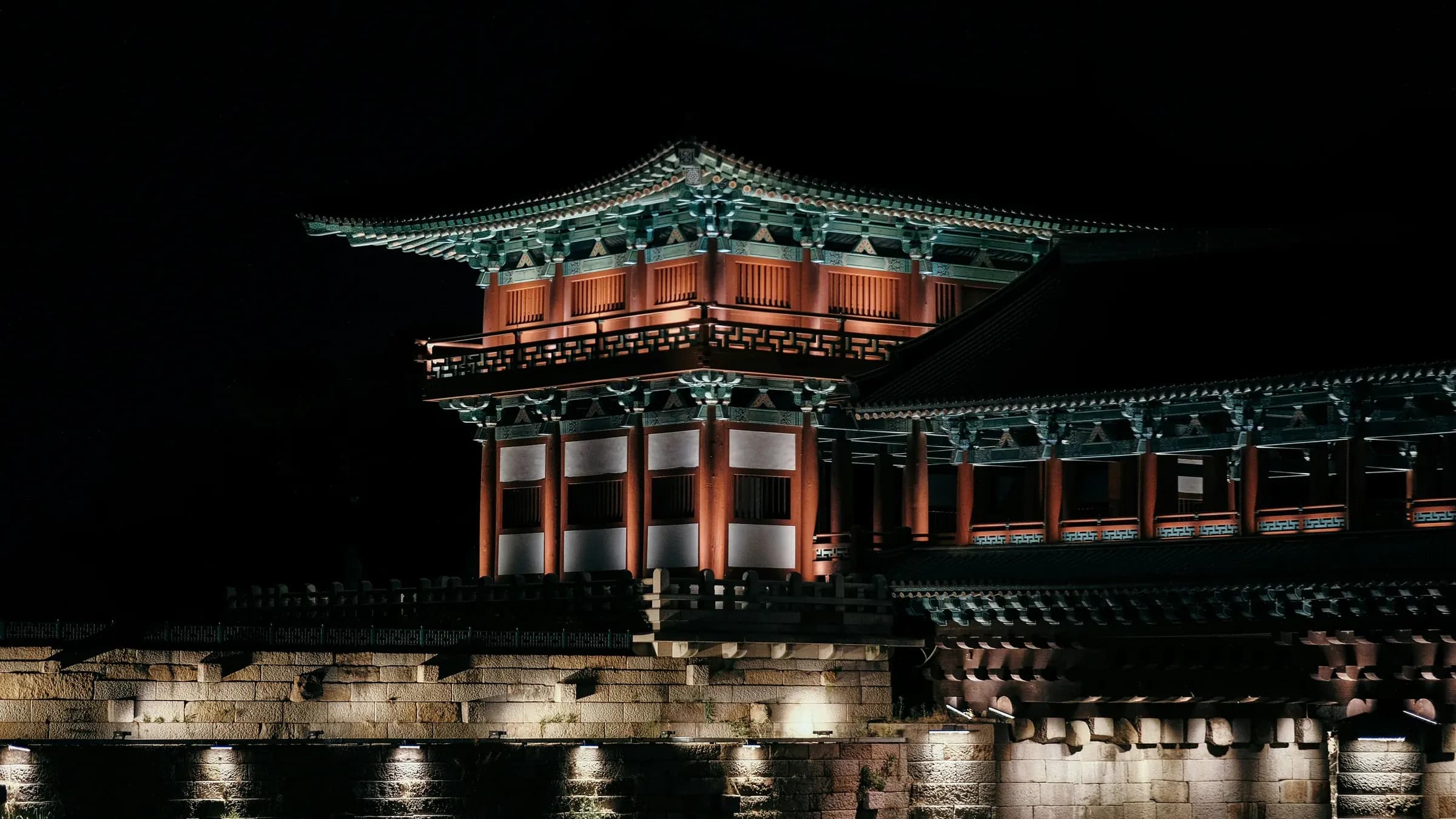 A Korean palace gate lit up at night against a black sky.