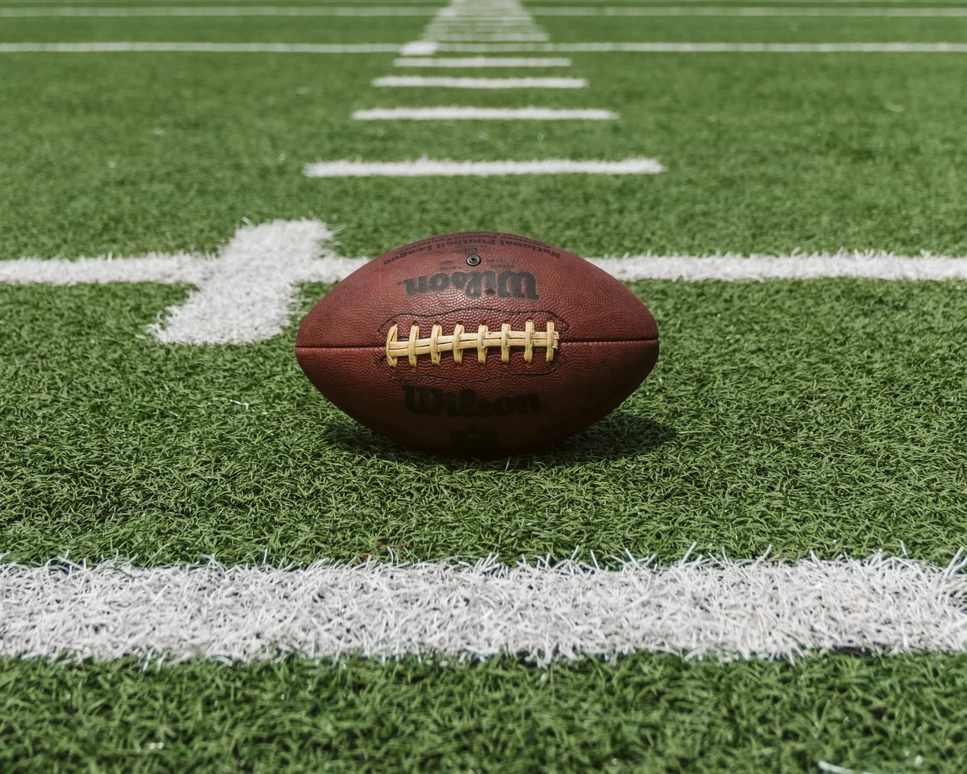 An American football resting on the turf between the yard lines of a football field.