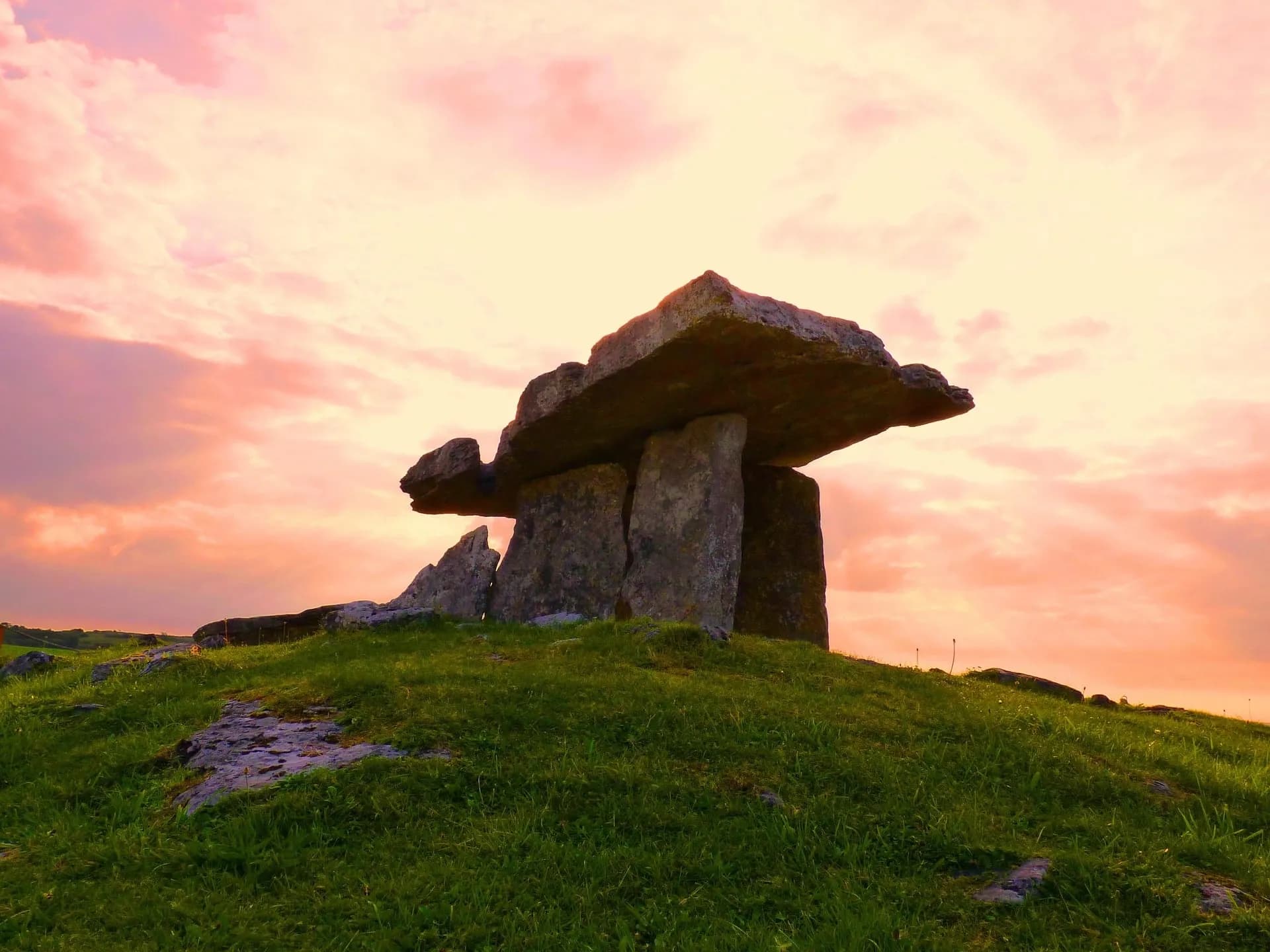 A large ancient stone dolmen stands on a grassy hill under a dramatic sunset sky, with pink and orange clouds illuminating the scene—a perfect highlight for Steelers in Dublin Travel Packages.