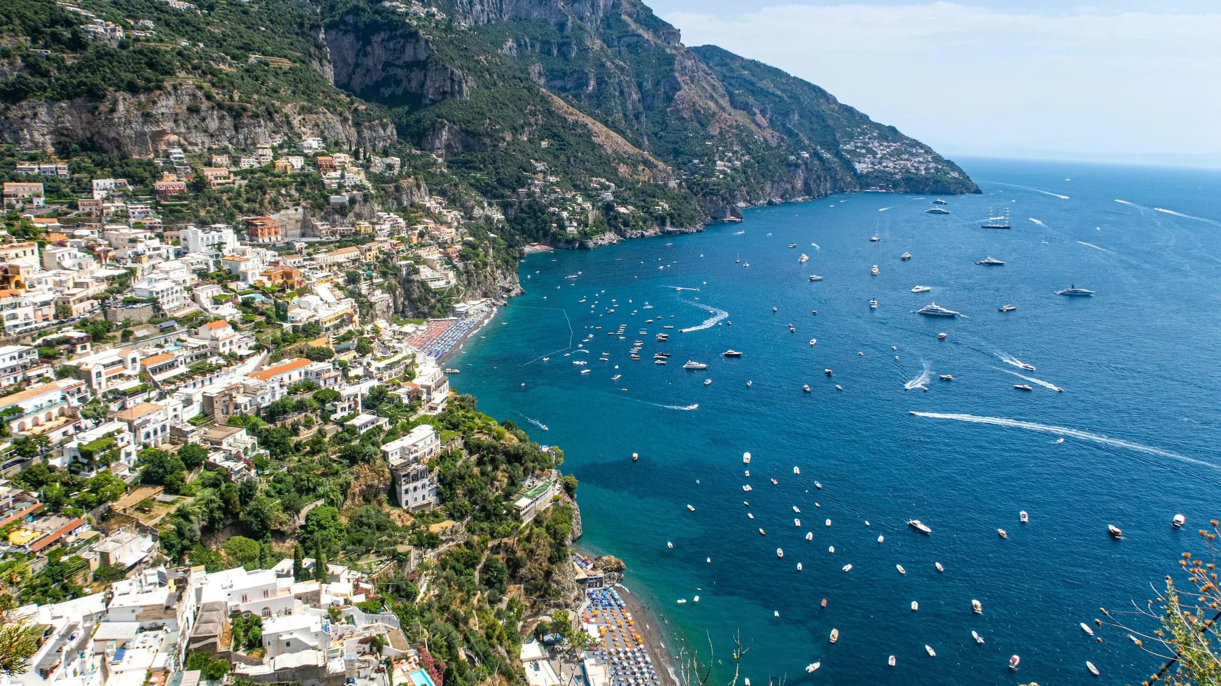Aerial view of Positano's pastel houses tumbling down to a beach and a bay full of boats on the Amalfi Coast.