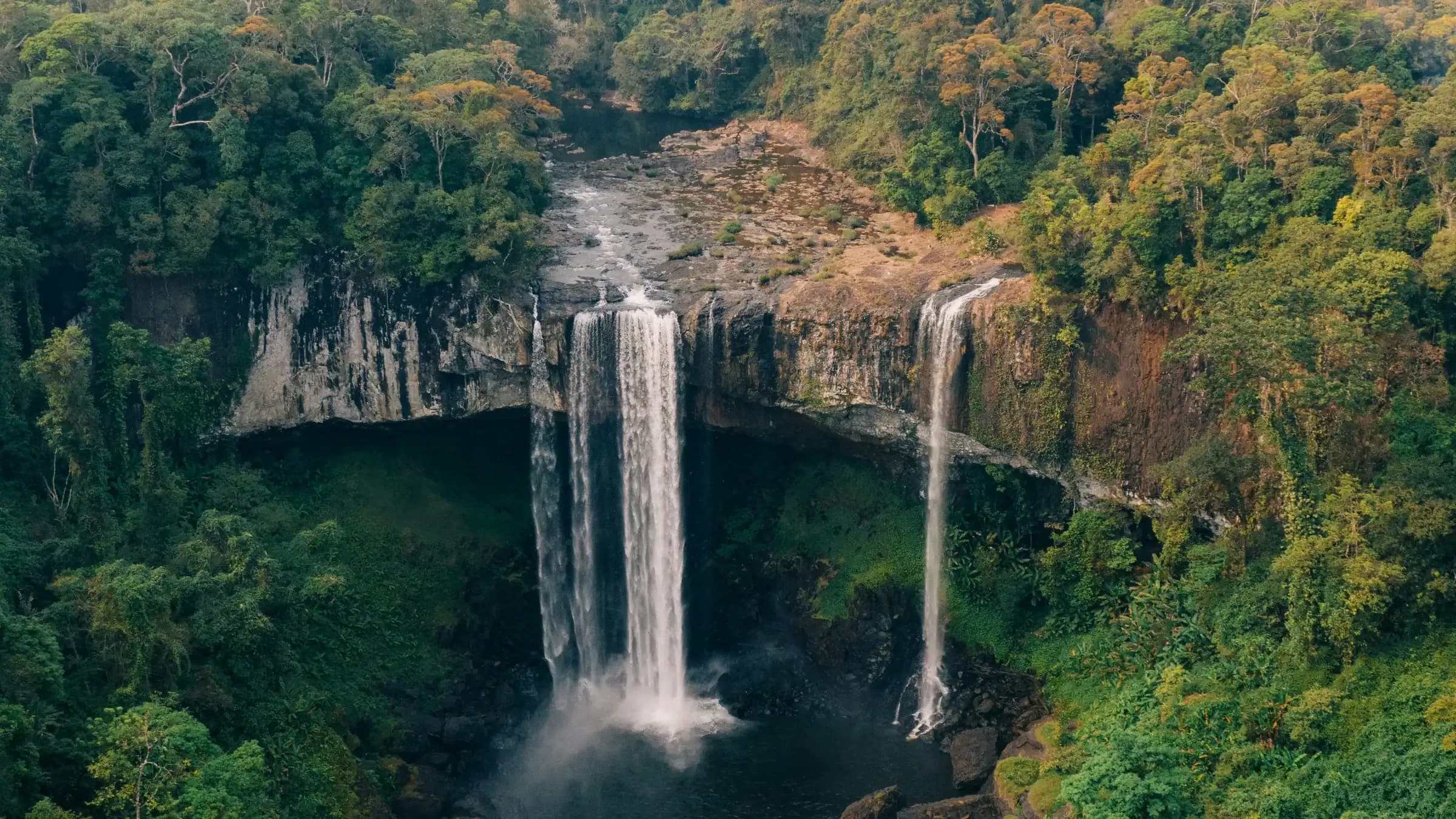A tall waterfall pouring over a cliff into a deep, jungle-covered gorge.