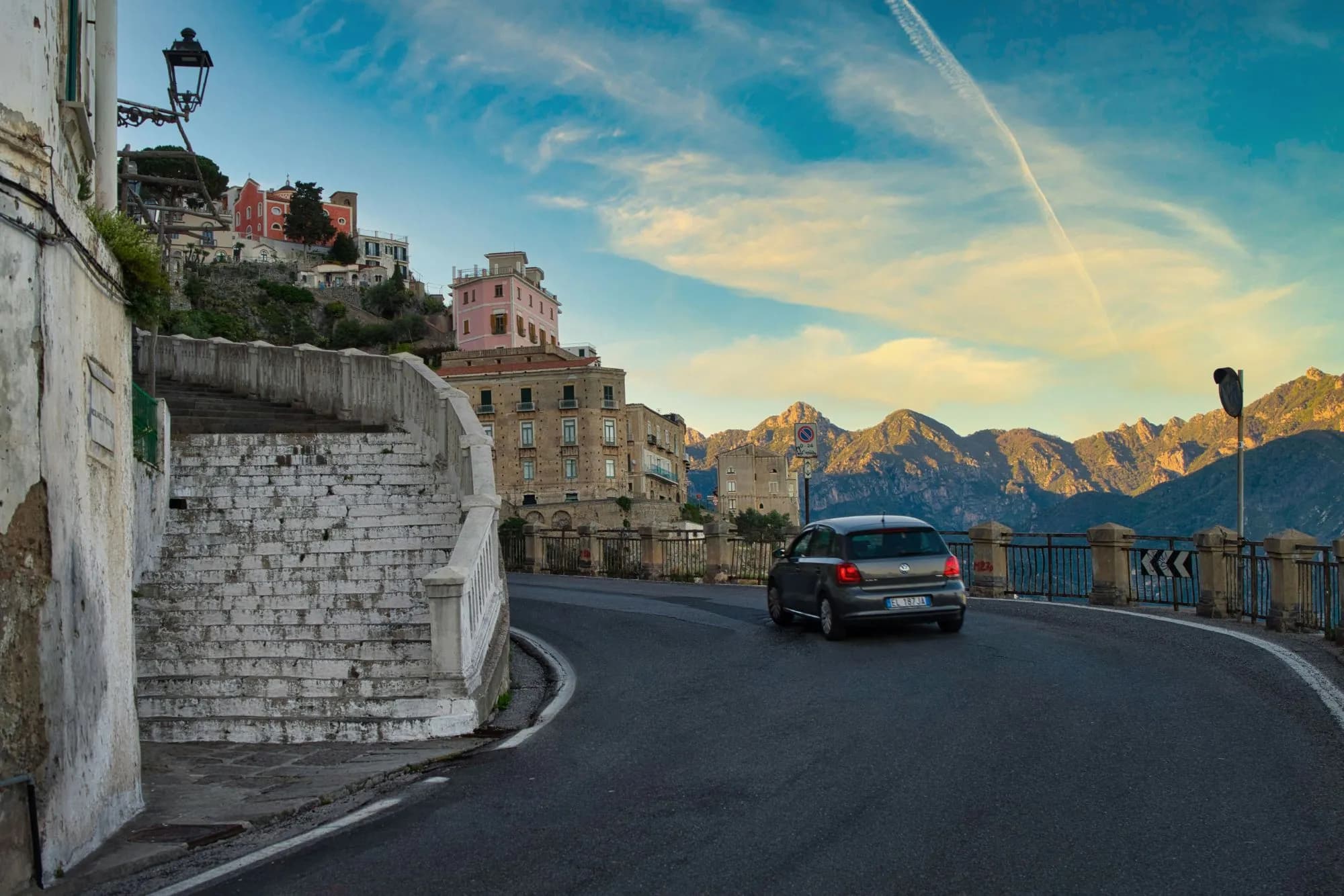 A car rounding a cliffside bend on the road to Ravello on the Amalfi Coast, with the Lattari Mountains behind
