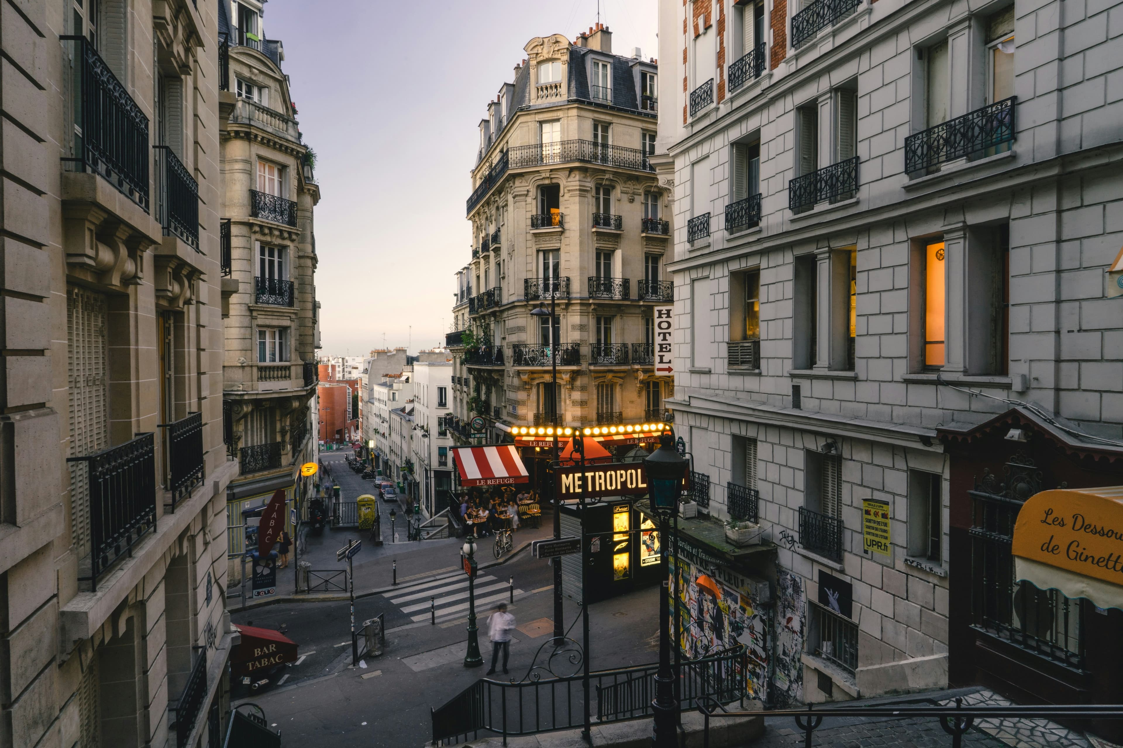 A scenic street view in Paris at dusk, showing classic Parisian buildings, glowing streetlights, and a Metropol sign above a staircase descending to the sidewalk—perfect inspiration for your Scotland and Ireland Tours 2026 adventure.