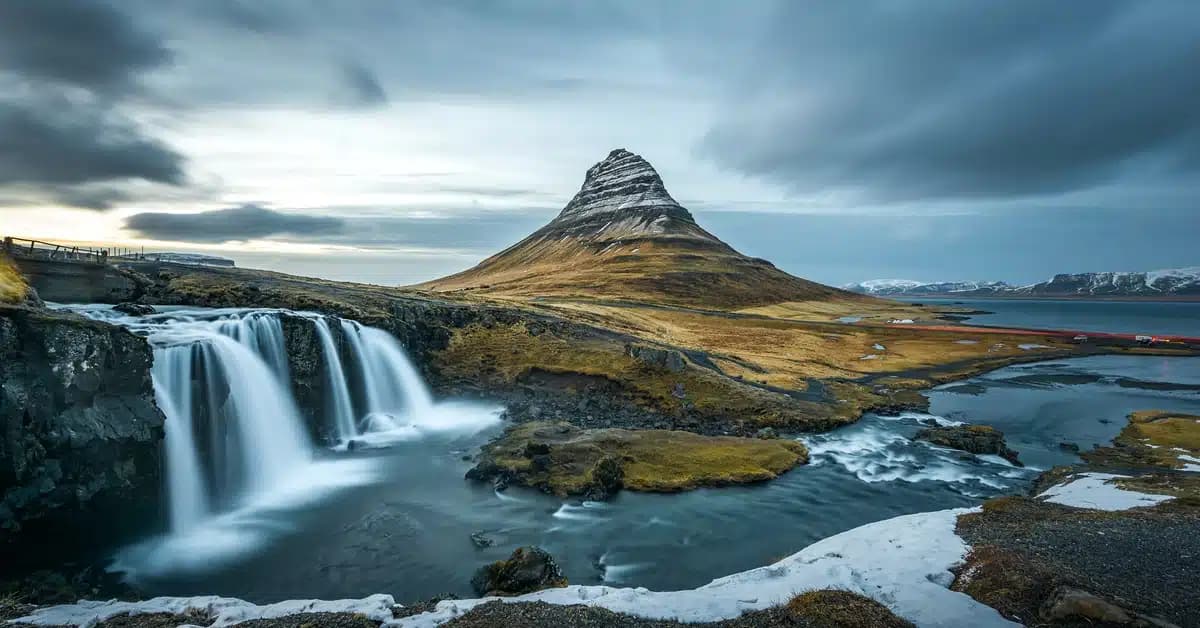 A gloomy, cloudy day in Iceland over the mountains. The waterfall drops into the base of the mountains.