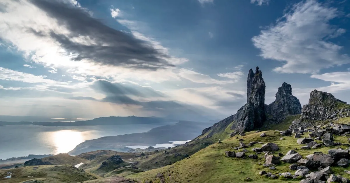 A sunrise view of the Isle of Skye with small clouds and rocks and cliffs at the edge of the water.