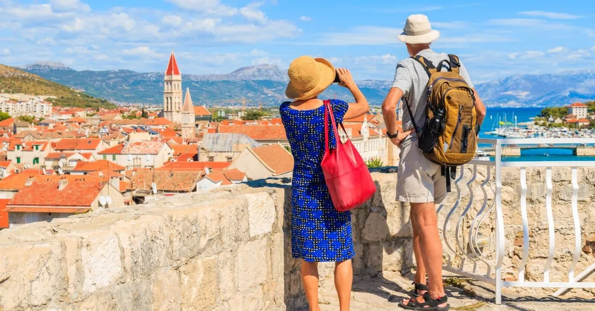 A couple on a European vacation tour dressed for a day of walking in Croatia. They're overlooking the landscape.