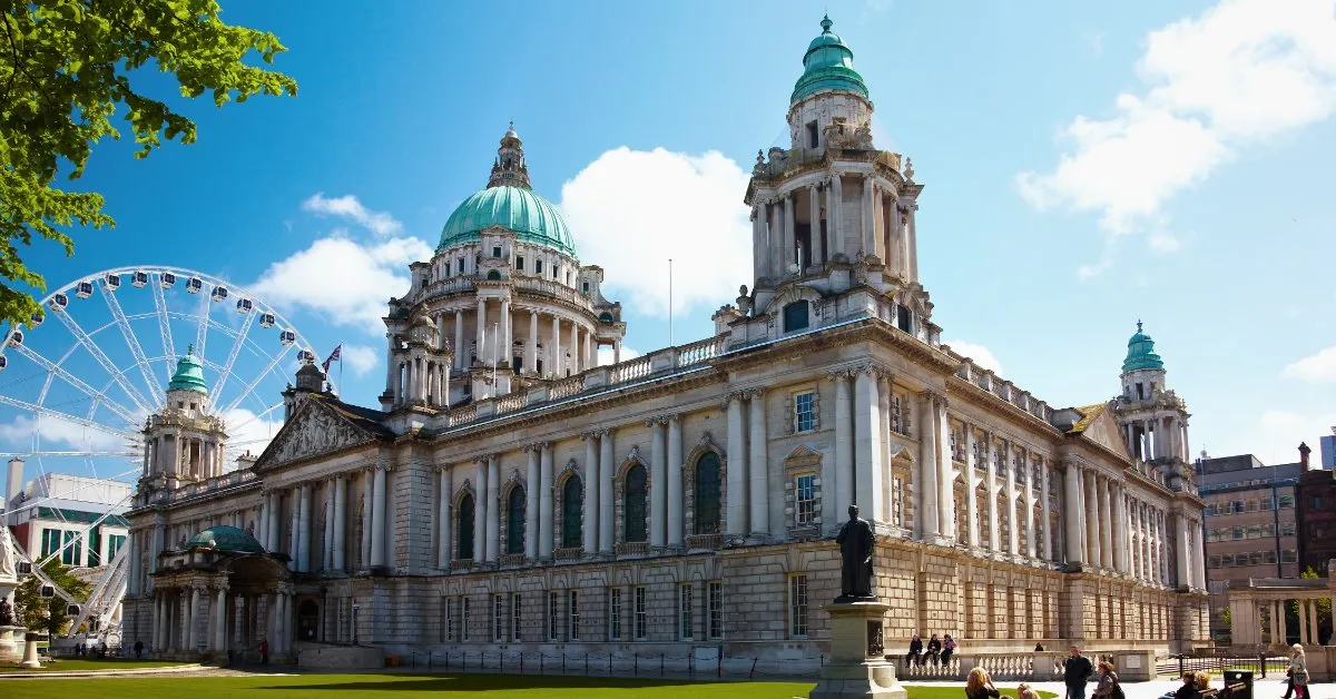 Belfast City Hall with its green copper domes under a blue sky, the Belfast Wheel turning beside it