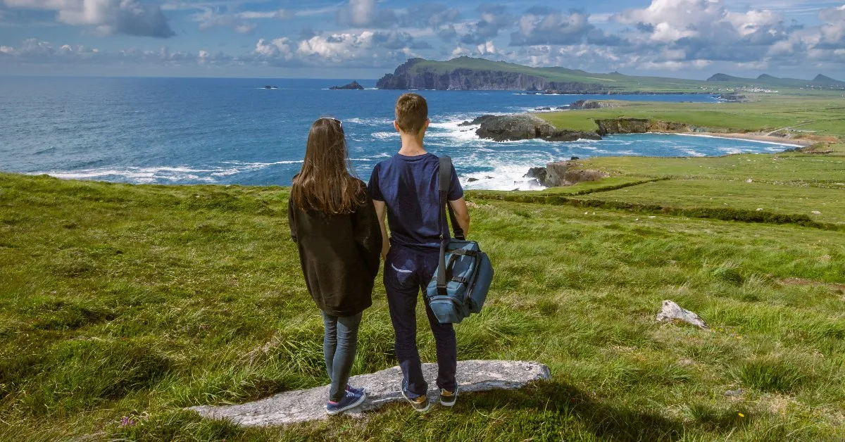A couple standing on a grassy clifftop looking out over the Atlantic coastline of the Dingle Peninsula in County Kerry