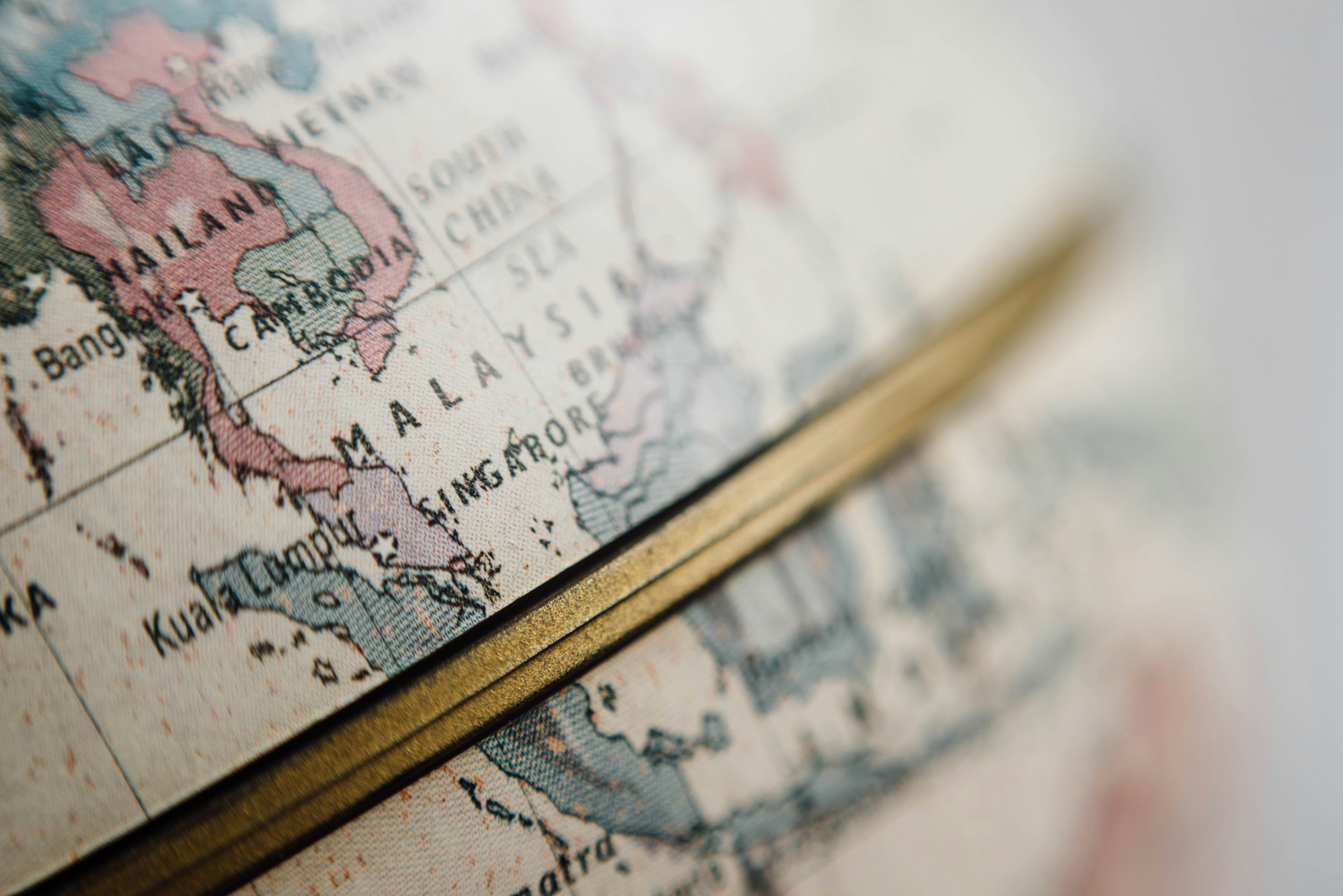 Close up of a globe showing Southeast Asia, including Malaysia, Singapore, Cambodia, and southern Thailand, with a brass axis bar running diagonally across the image.