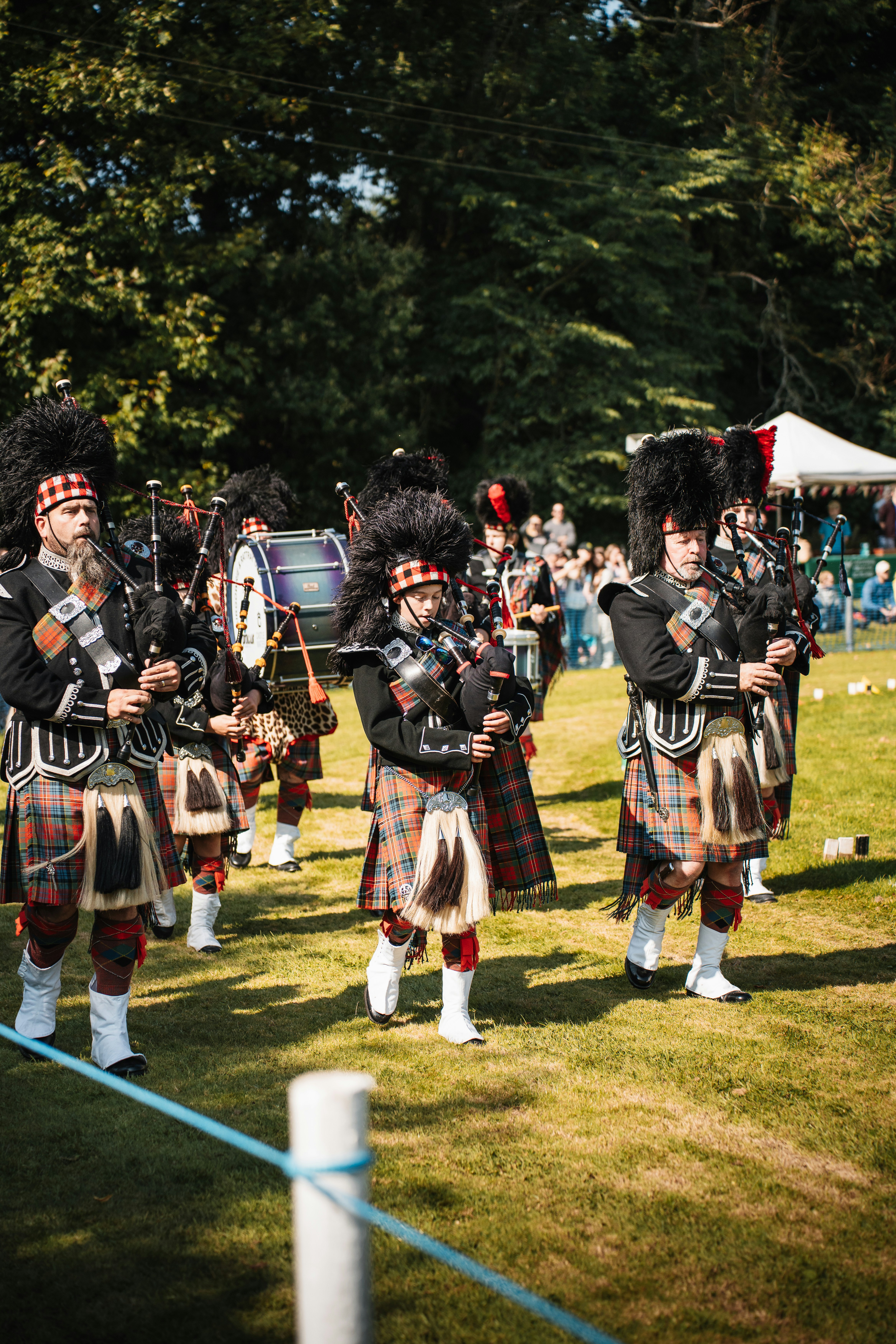 A group of bagpipers in traditional Scottish attire, including kilts and feathered hats, perform outdoors on a sunny day as a crowd gathers, reminiscent of the excitement at a Vikings vs Steelers 2025 event.