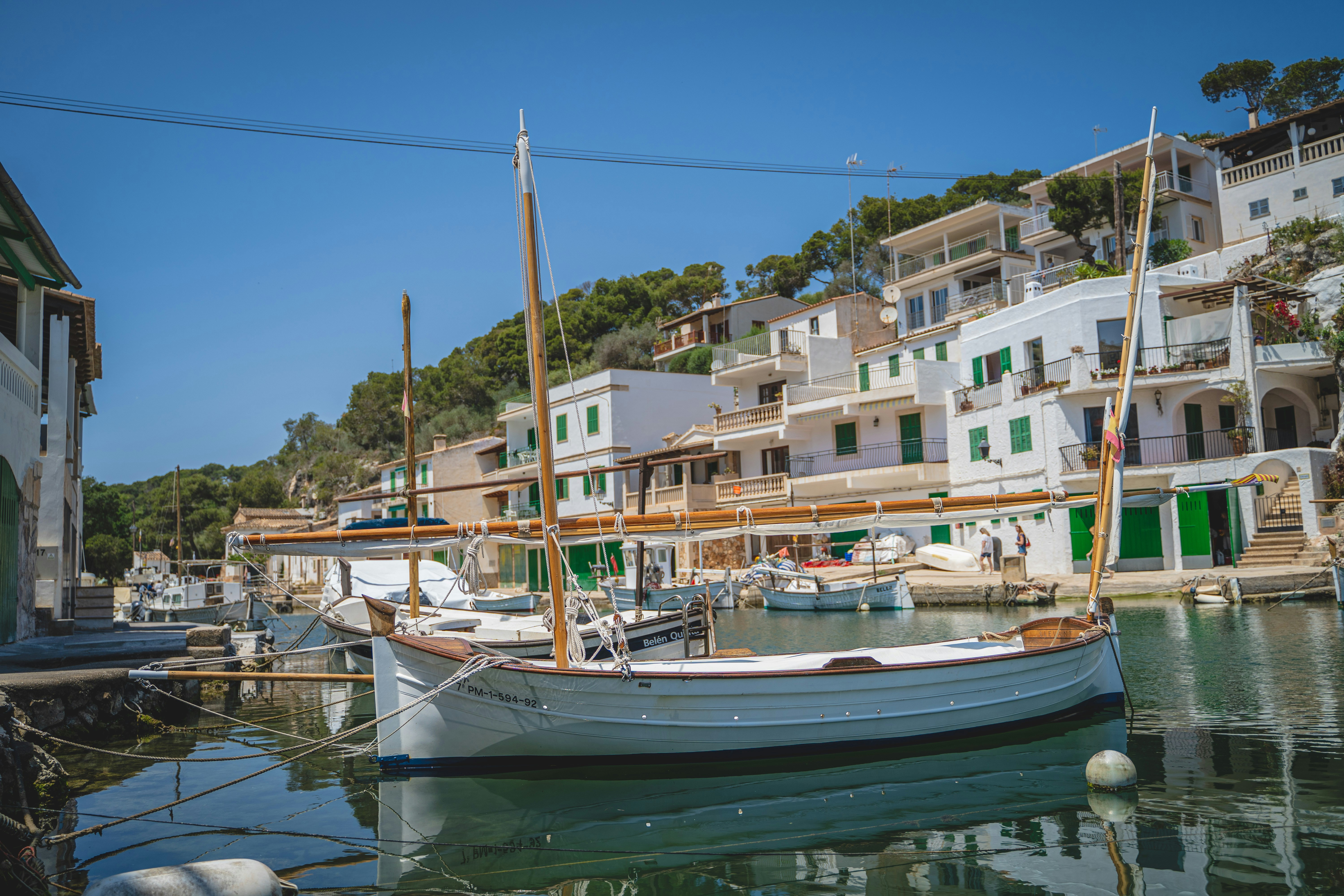 A traditional wooden boat floats on calm water in a small harbor, surrounded by white Mediterranean style buildings with green shutters and doors—an idyllic scene reminiscent of our France and Switzerland trips, under a clear blue sky.