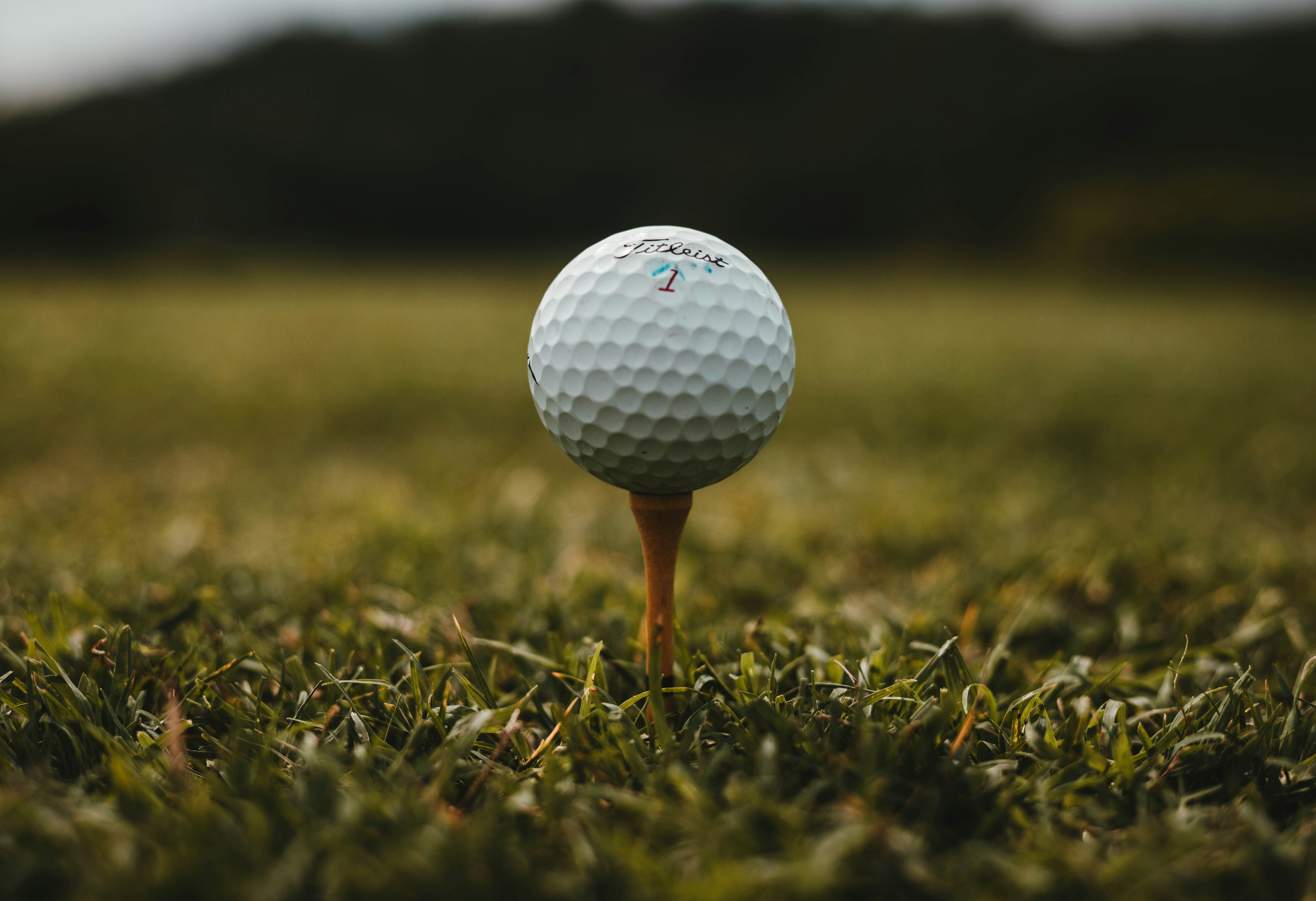 A close up of a white golf ball on a wooden tee, set on green grass with a blurred dark background—perfect for dreaming about your next swing!