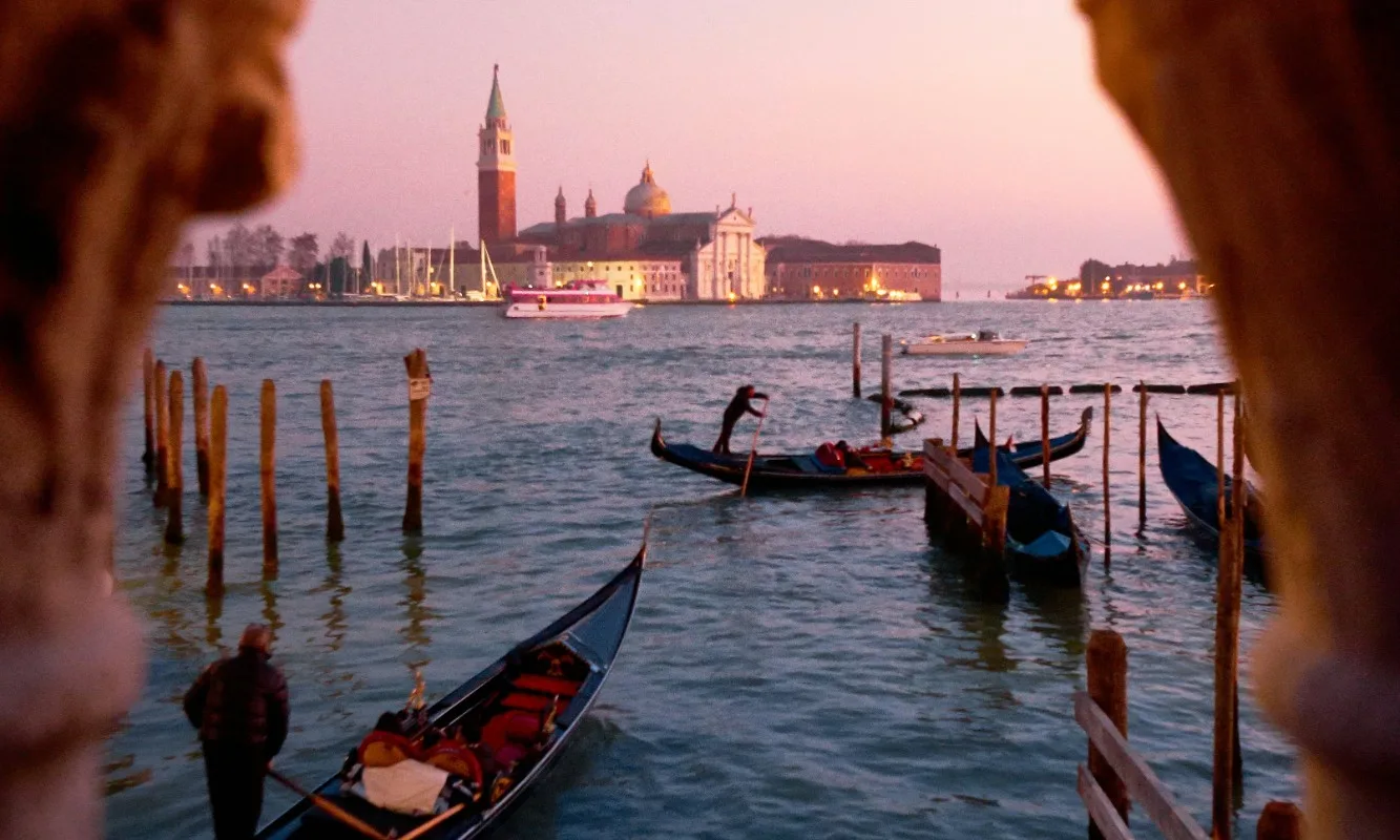 Gondolas on the Venice lagoon at dusk, with the church of San Giorgio Maggiore seen through a stone arch