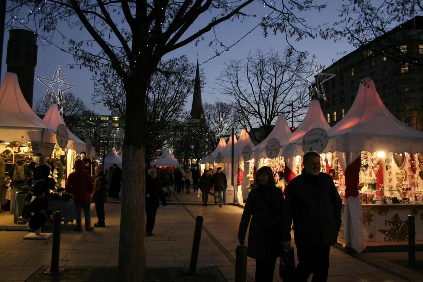German Christmas market at blue hour with illuminated stalls, star lights and shoppers