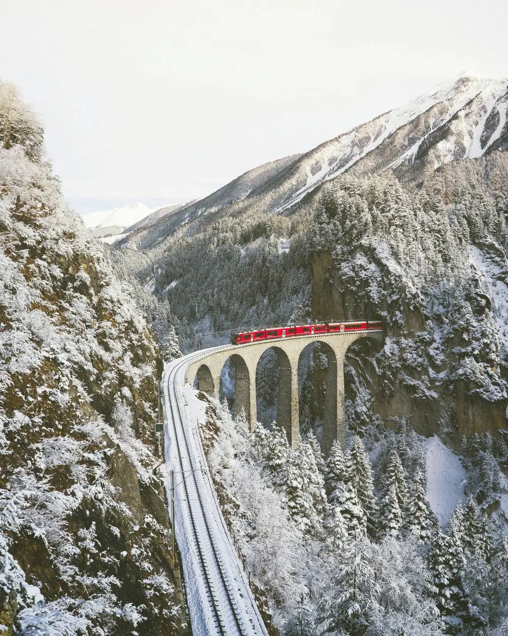 A red Rhaetian Railway train crossing the stone arches of the Landwasser Viaduct in a snowy Swiss gorge